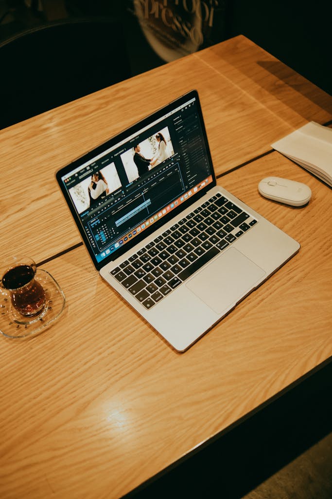 A laptop on a wooden table in a coffee shop, displaying video editing software for creative work.