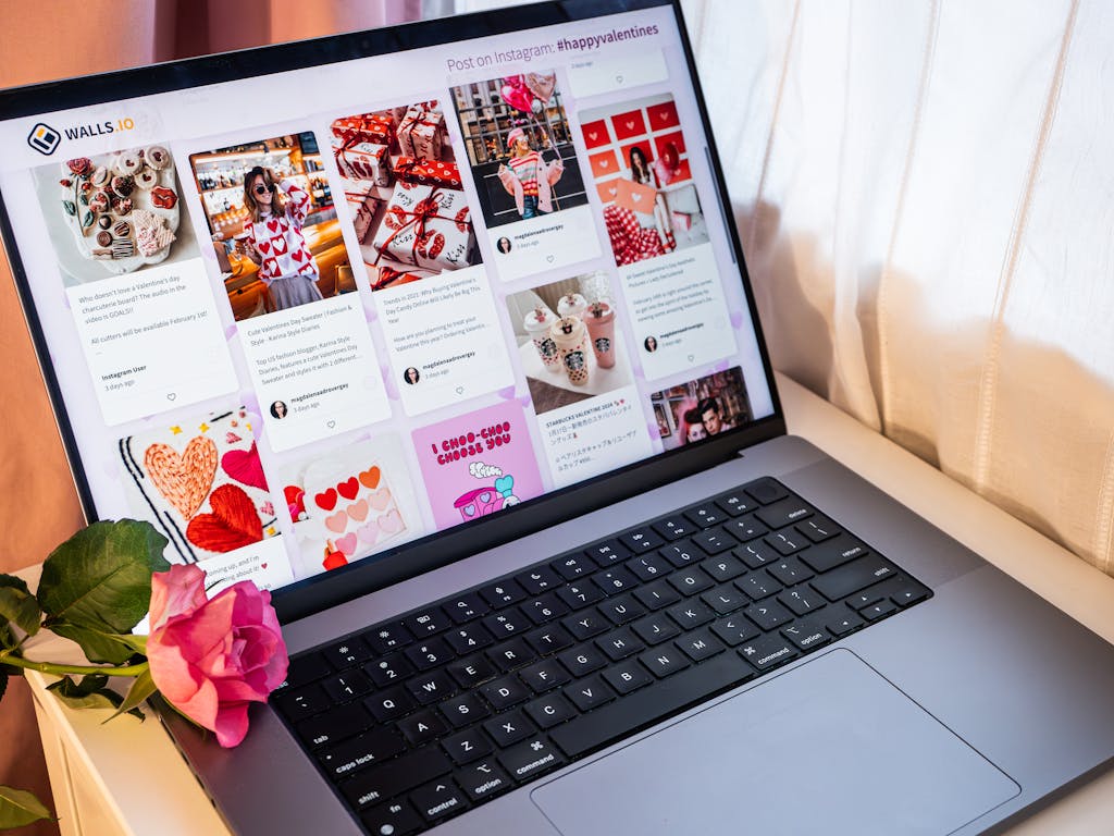 A laptop showcasing a social media wall with vibrant posts beside a pink rose.