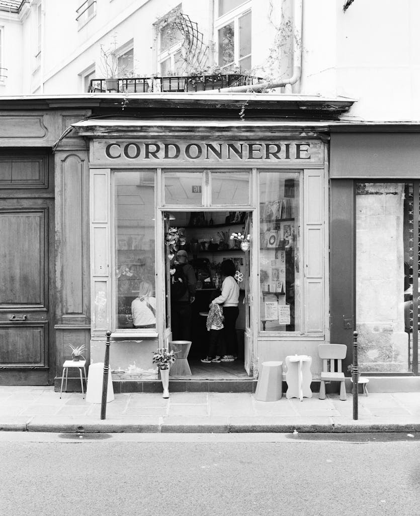 Black and white image of a Parisian shoe repair shopfront with people inside.